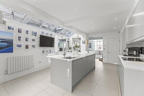 A modern kitchen with a central island, white cabinetry, and a large window above the sink. - Stylish Windsor Home | Hot Tub | Town Centre (Windsor)