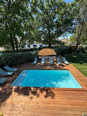 Ein Schwimmbecken mit Liegestühlen, umgeben von Bäumen und einer Holzterrasse.