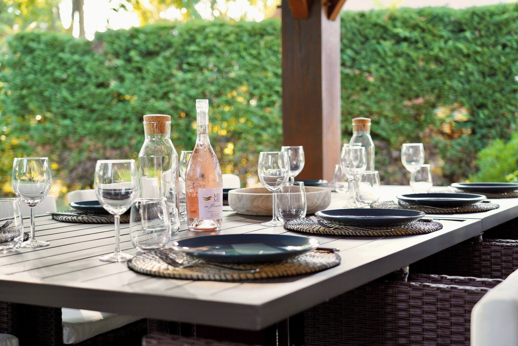 Mesa de comedor al aire libre con vasos transparentes, platos y una botella.