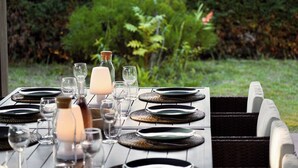 An outdoor dining table set with plates, glasses, and a candle, surrounded by lush greenery. - Villa Bonamour - Capbreton - Pool - Port - Beach (Capbreton)