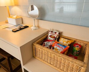 A kitchen counter with a basket of snacks, a tissue box, a remote control, and a mirror. - Sun and Moon - Bed and Bistro (Bangkok)