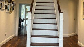 Una escalera con barandillas blancas y escalones de madera oscura, que conduce a un rellano con un cuadro en blanco y negro.