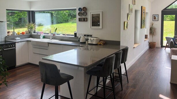 Una cocina moderna con una isla grande, taburetes de bar, un fregadero y una ventana con vistas a un jardín.