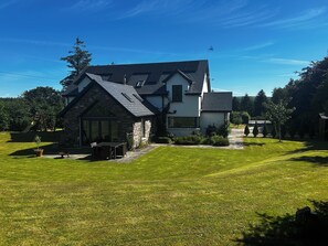 Ein modernes Haus mit Naturstein-Fassade, einem großen Rasen und einem Spielbereich für Kinder.