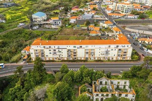 Eine Vogelperspektive auf ein Wohngebiet mit einem markanten, mehrstöckigen Gebäude mit Balkonen, einer Straße mit Fahrzeugen und umliegender Bepflanzung.