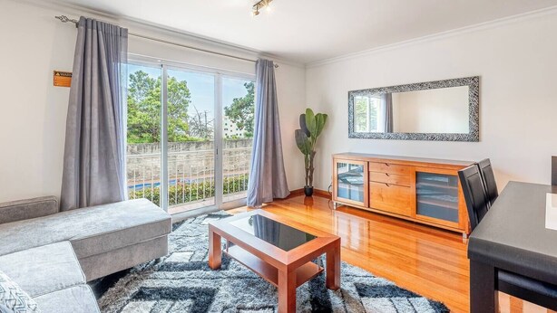 Ein modernes Wohnzimmer mit einer Couch, einem Glastisch, einem Holzschrank und einem Esstisch.