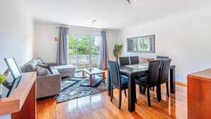 Ein modernes Wohnzimmer mit einer Couch, einem Couchtisch, einem Esstisch mit Stühlen und einem großen Fenster mit Vorhängen.