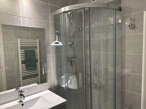 Ein modernes Badezimmer mit einer gläsernen Duschkabine, einem weißen Waschbecken und einem Handtuchhalter.