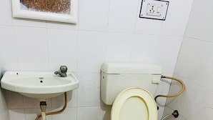 Un baño pequeño y sencillo con inodoro, lavamanos y un enchufe a la vista en la pared.