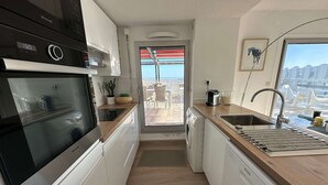A compact kitchen with a dishwasher, a coffee maker, and a view of the balcony. - Beautiful 2-bedroom with terrace near beach and shops, parking included (La Grande-Motte)