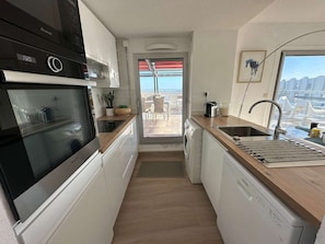 Eine kompakte Küche mit Spülmaschine, Kaffeemaschine und Blick auf den Balkon.