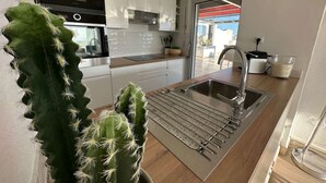 A modern kitchen with white cabinets, a stainless steel sink, and a microwave. - Beautiful 2-bedroom with terrace near beach and shops, parking included (La Grande-Motte)
