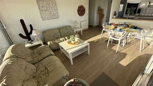 A living room with a sofa, coffee table, and chairs, a dining area with a table and chairs, a kitchen with modern appliances, and a cactus decoration. - Beautiful 2-bedroom with terrace near beach and shops, parking included (La Grande-Motte)