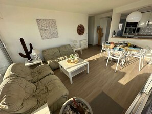 Ein Wohnzimmer mit Sofa, Couchtisch und Sesseln, ein Essbereich mit Tisch und Stühlen, eine Küche mit modernen Geräten und eine Zimmerpflanze, ein Kaktus.