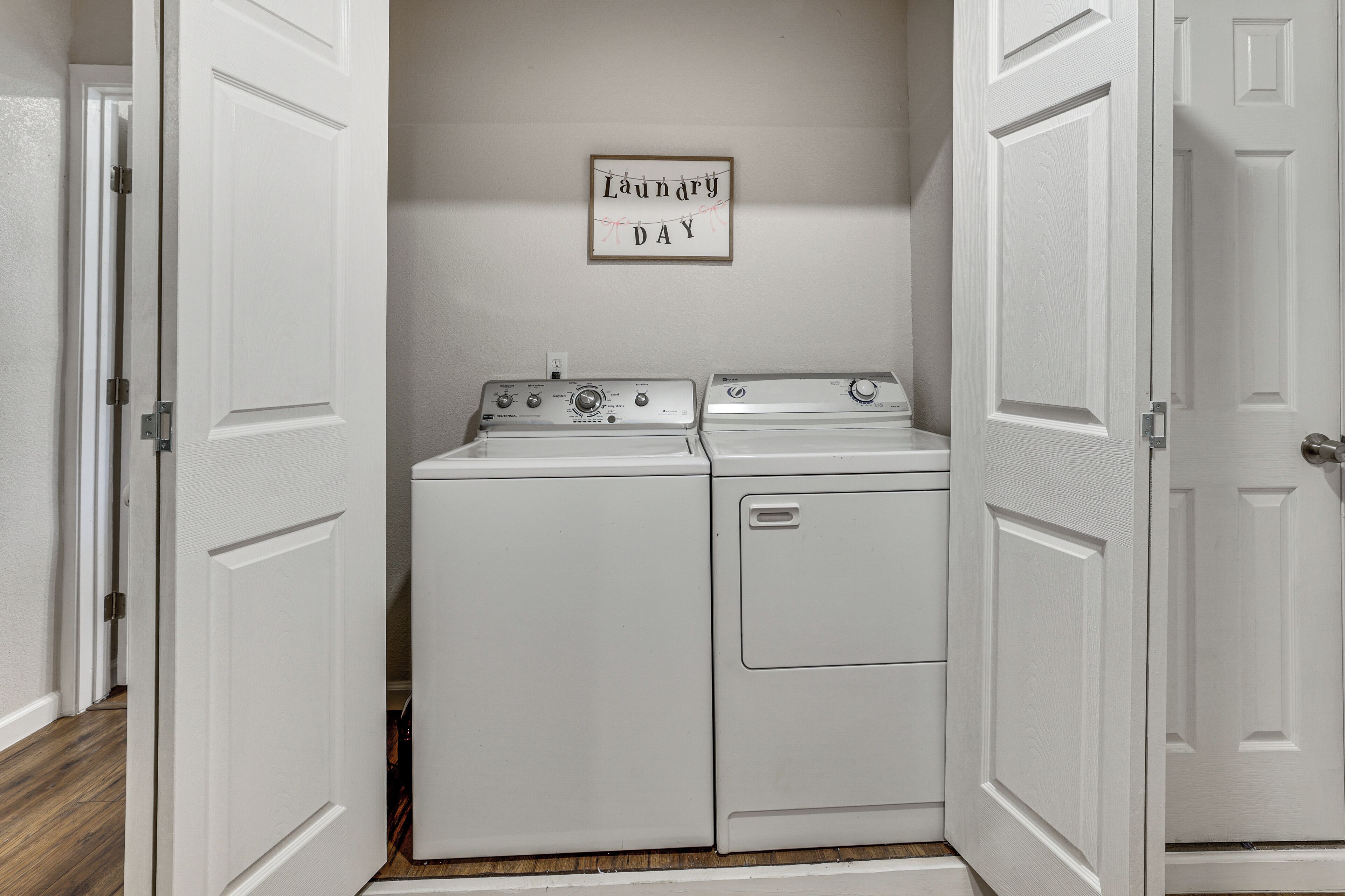 A laundry room with two stacked washers and dryers, a sign above them, and white doors.