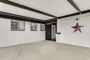 Un espacio exterior techado con una pared blanca, una puerta decorada con una estrella y una ventana con persianas.