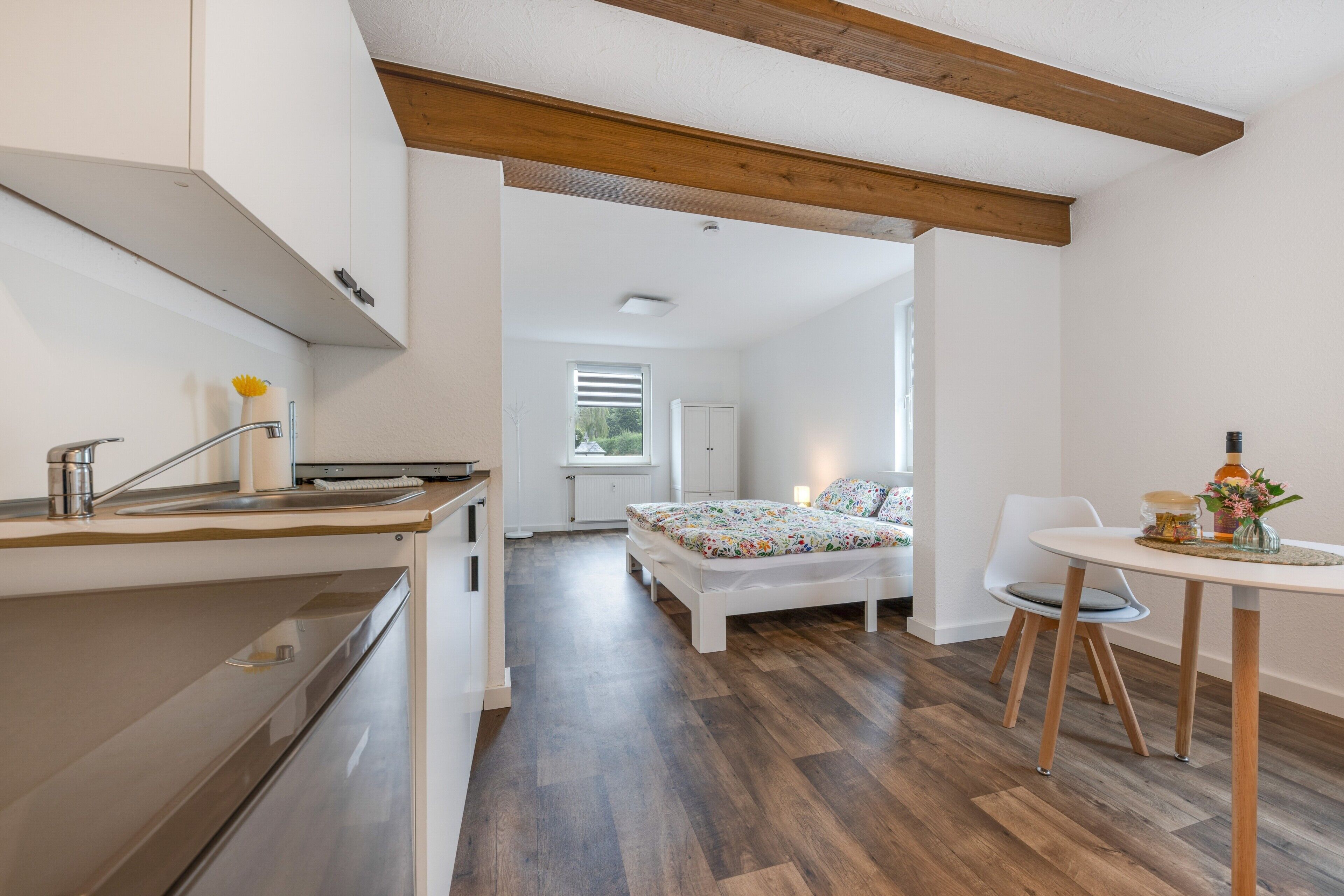 A modern kitchen with a built-in oven, a dining area with a table and chairs, and a bedroom with a bed and window.