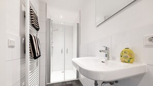 A modern bathroom with a white sink, a glass shower enclosure, and a towel rack with striped towels.