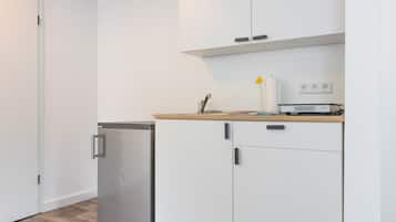 A compact kitchen with white cabinets, a small refrigerator, and a countertop with a sink and a lamp.