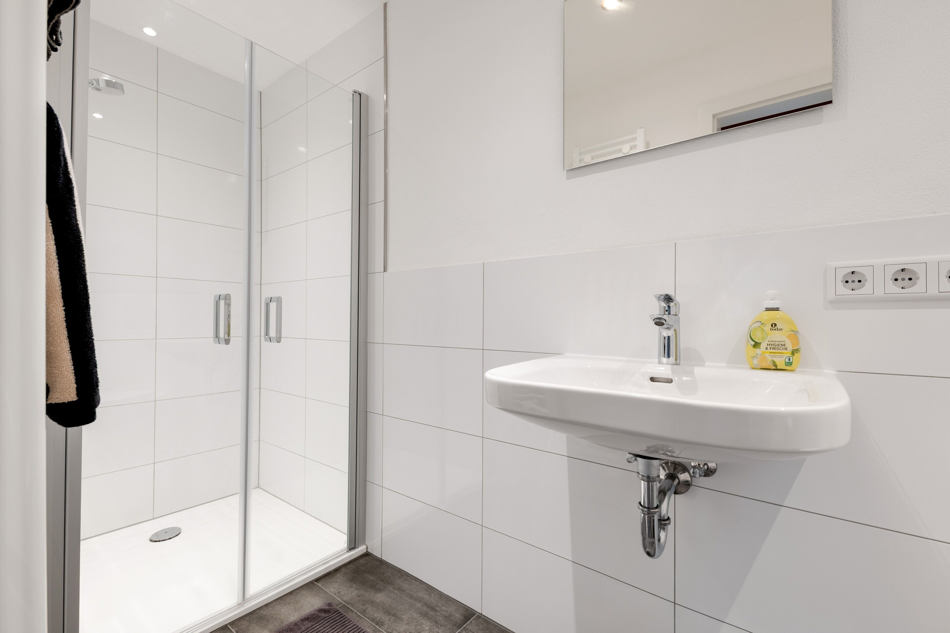 Ein modernes Badezimmer mit Duschkabine aus Glas, einem weißen Waschbecken mit Armatur und einem Spiegel darüber.