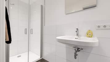 Ein modernes Badezimmer mit Duschkabine aus Glas, einem weißen Waschbecken mit Armatur und einem Spiegel darüber.