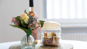 En glasvas med blommor, en flaska och en burk med godis, placerade på en vävd bordsduk.