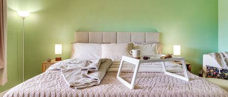 Una cama bien hecha con un edredón acolchado, una mesita de noche con una lámpara y un cuadro en la pared.