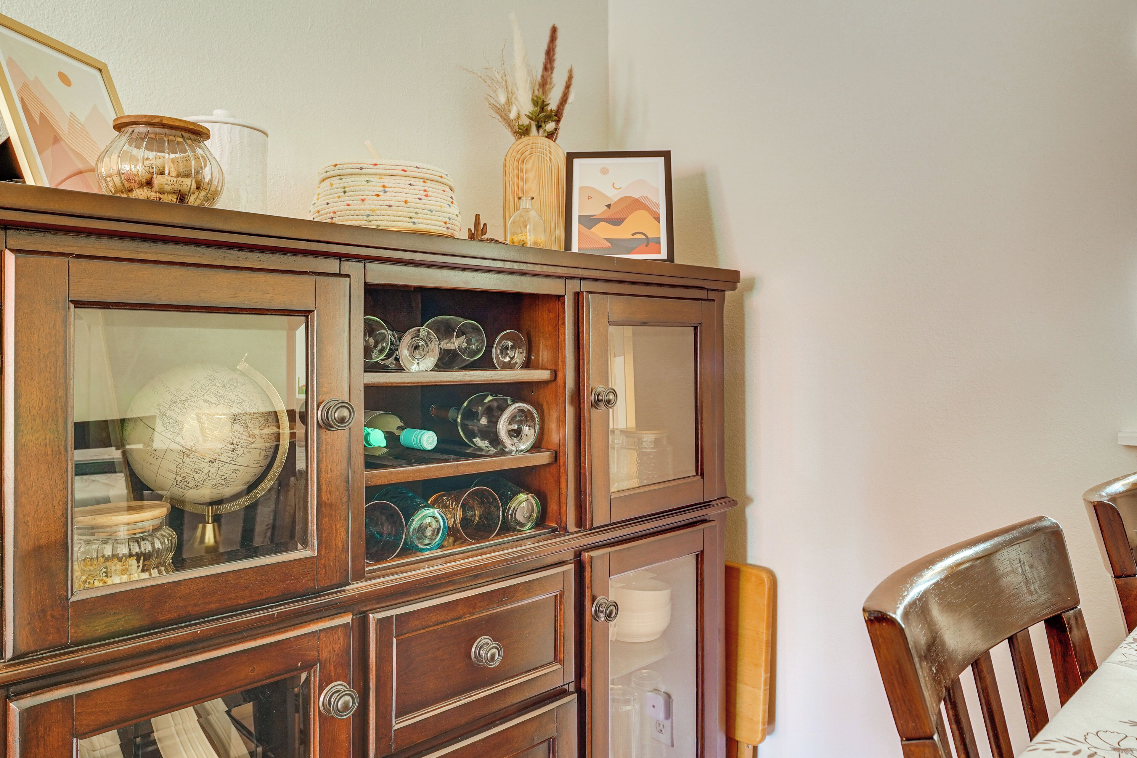 A wooden cabinet with glass doors containing various glassware and a globe.