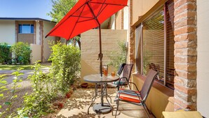 A patio with a table and chairs, a red umbrella, and a brick wall. - Steps to Fashion Square! Condo w/ Patio & Pool (Scottsdale)