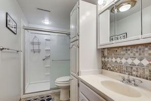 Baño con ducha, inodoro, lavabo y un espejo sobre el lavabo.