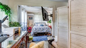 Ein Schlafzimmer mit einem Bett, einem Schreibtisch, einem Drucker und einem an der Wand befestigten Fernseher.