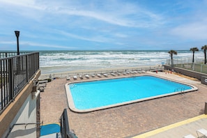 A swimming pool with a view of the ocean, a brick deck, and a railing.