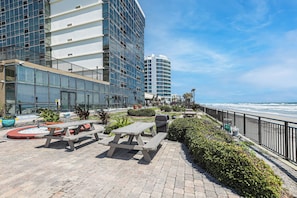 A beachfront patio with picnic tables, a trash bin, and a view of the ocean.