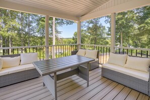 A covered outdoor seating area with wicker furniture and a table, surrounded by a railing. - On 4+ Acres! Modern Home w/ Lake Access in Orange (Orange)