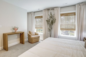A bedroom with a large bed, a wooden console table, a chair, and a window with curtains.