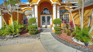 A house with a yellow facade, white columns, and a central entrance with a glass door. - Games, Outdoor Kitchen: Port St Lucie Family Home (Port Saint Lucie)