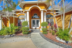 A house with a yellow facade, white columns, and a central entrance with a glass door.
