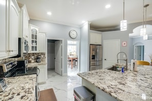 A kitchen with white cabinets, a marble countertop, a stainless steel refrigerator, and a clock on the wall.