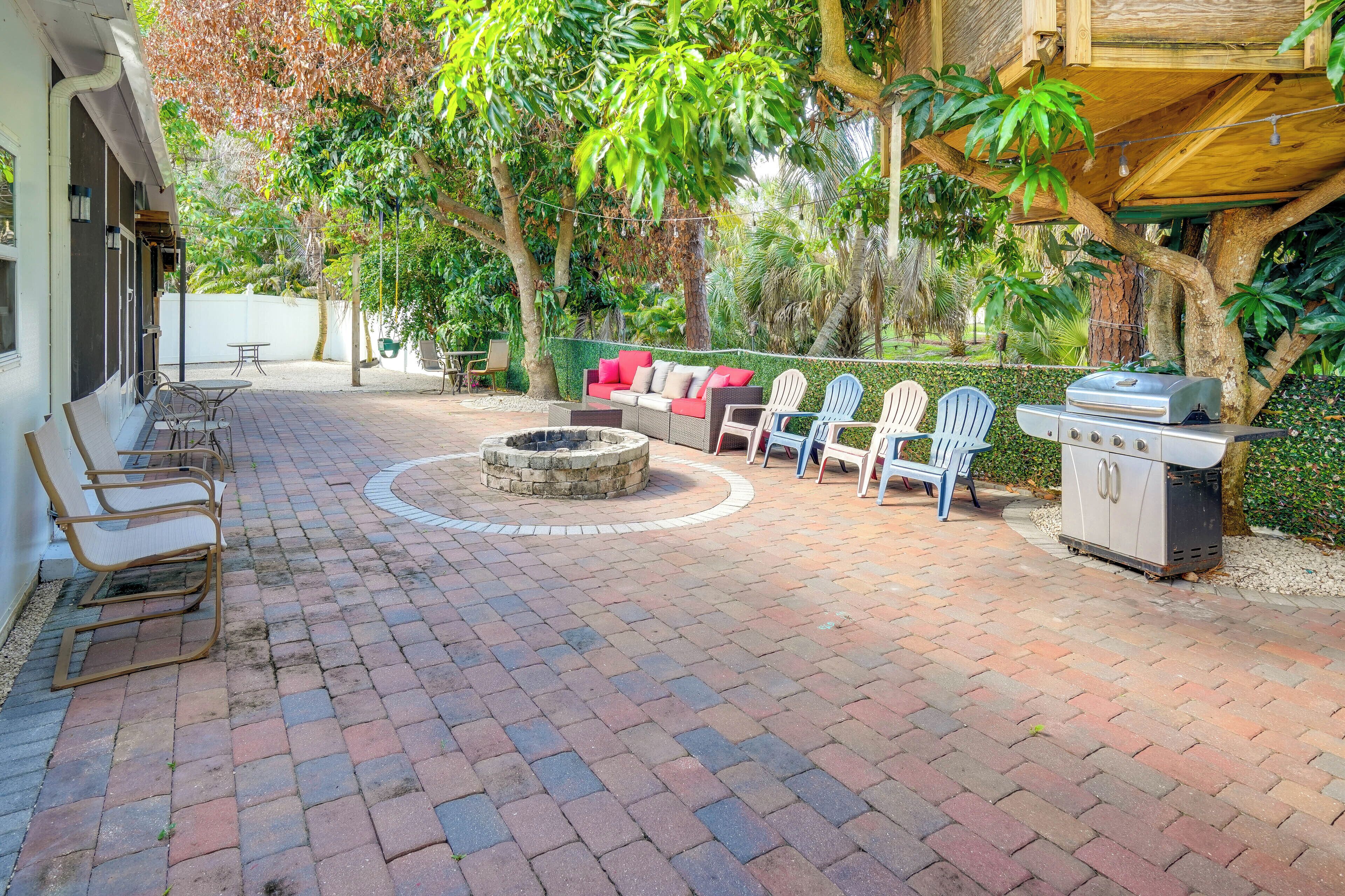 A patio with brick flooring, a fire pit, outdoor seating, and a grill area.
