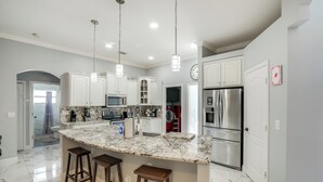 A modern kitchen with white cabinets, a marble island with stools, stainless steel appliances, and pendant lighting. - Games, Outdoor Kitchen: Port St Lucie Family Home (Port Saint Lucie)