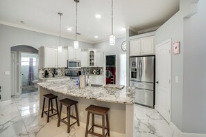 A modern kitchen with white cabinets, a marble island with stools, stainless steel appliances, and pendant lighting. - Games, Outdoor Kitchen: Port St Lucie Family Home (Port Saint Lucie)