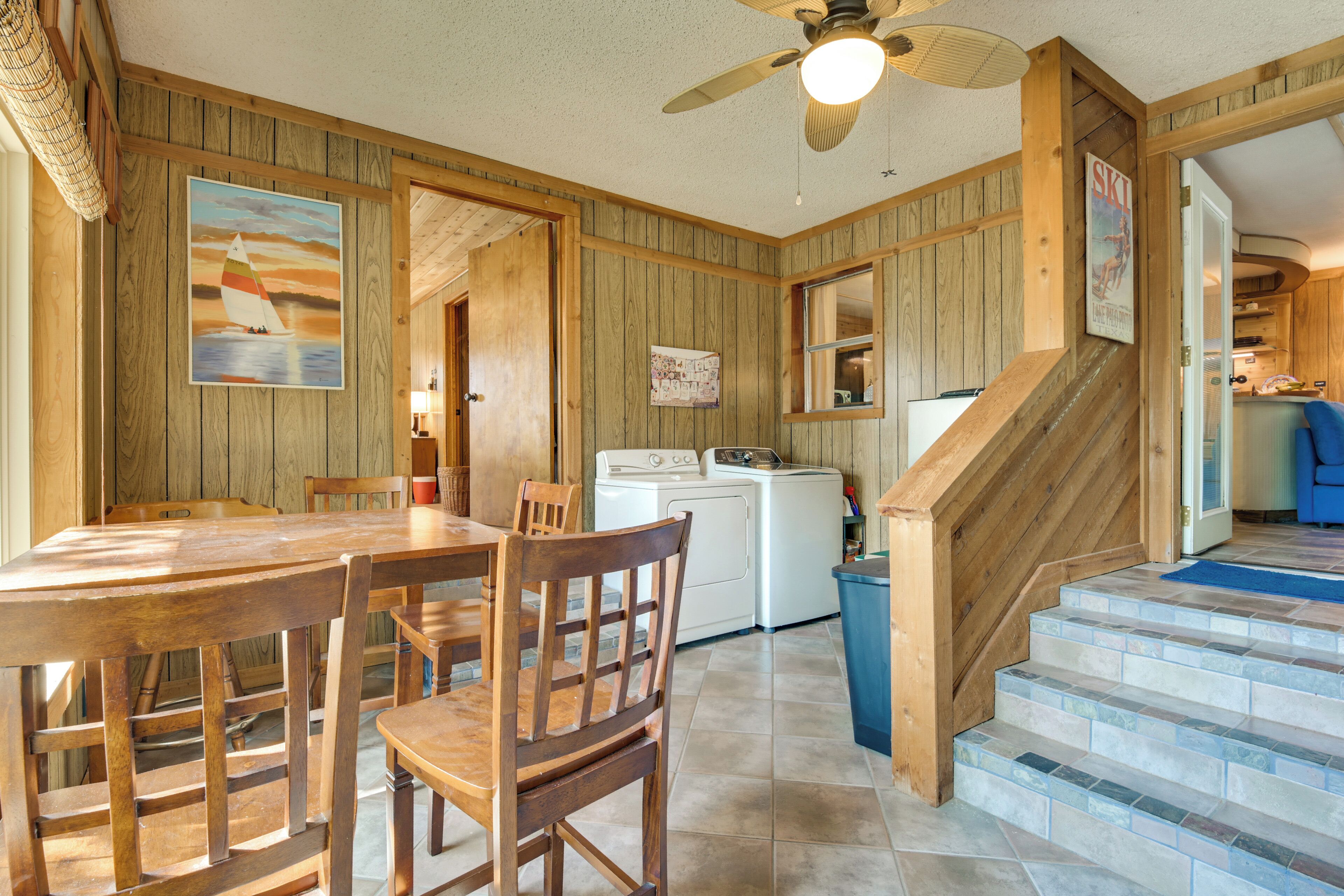 A wooden interior with a dining table, chairs, a ceiling fan, a washing machine, and a staircase.