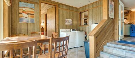 A wooden interior with a dining table, chairs, a ceiling fan, a washing machine, and a staircase.