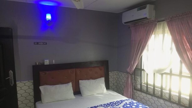 A hotel room with a bed, a 'NO SMOKING' sign, an air conditioning unit, and a window with curtains.