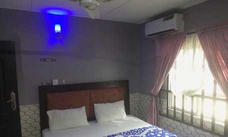 A hotel room with a bed, a 'NO SMOKING' sign, an air conditioning unit, and a window with curtains.. Pleasure rest hotel and suites