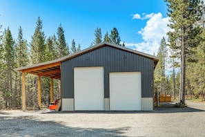 Ein eingeschossiges Gebäude aus Metall mit zwei großen Garagentoren, umgeben von einem Wald.