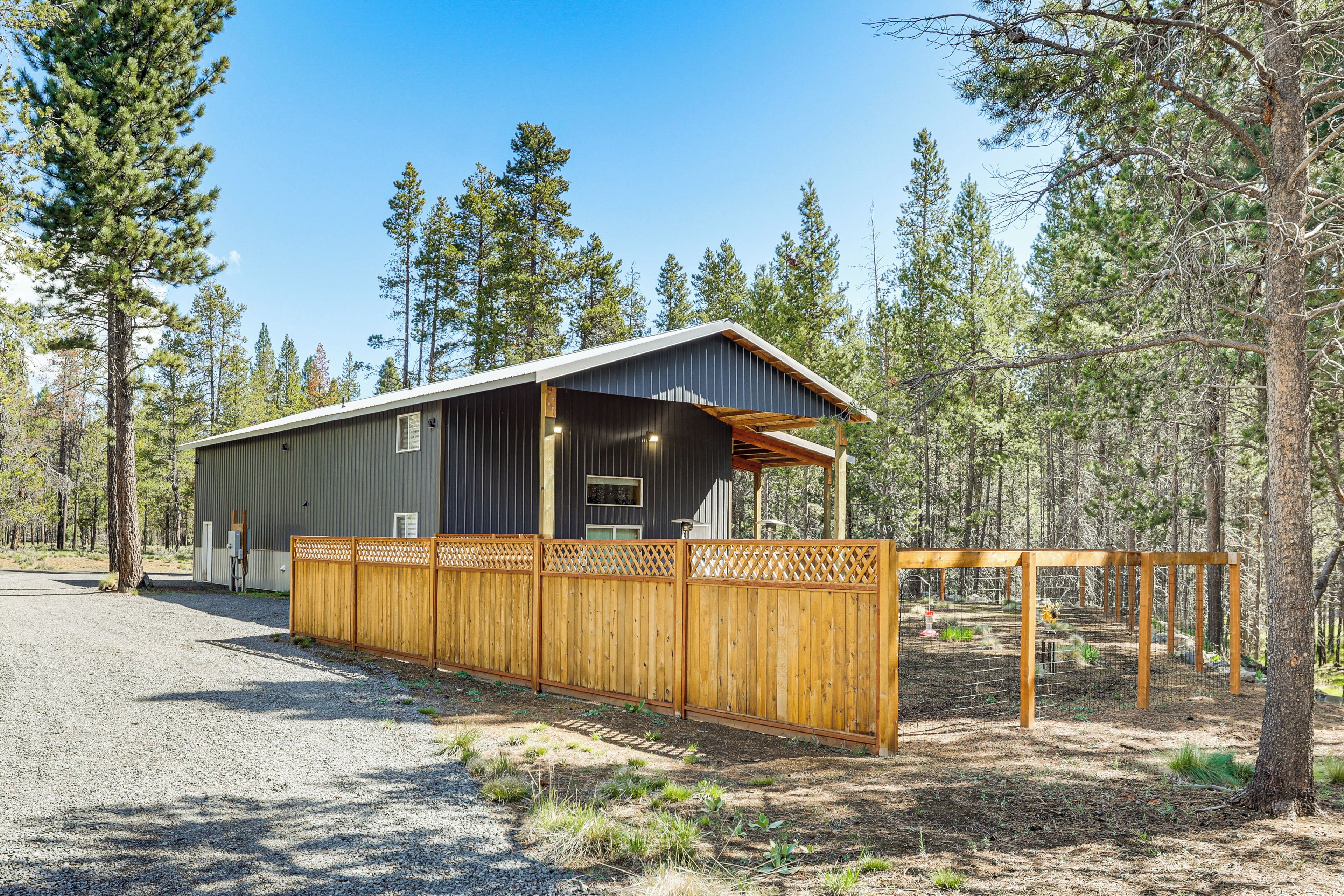 A single-story building with a dark exterior, a wooden fence, and a gravel driveway.