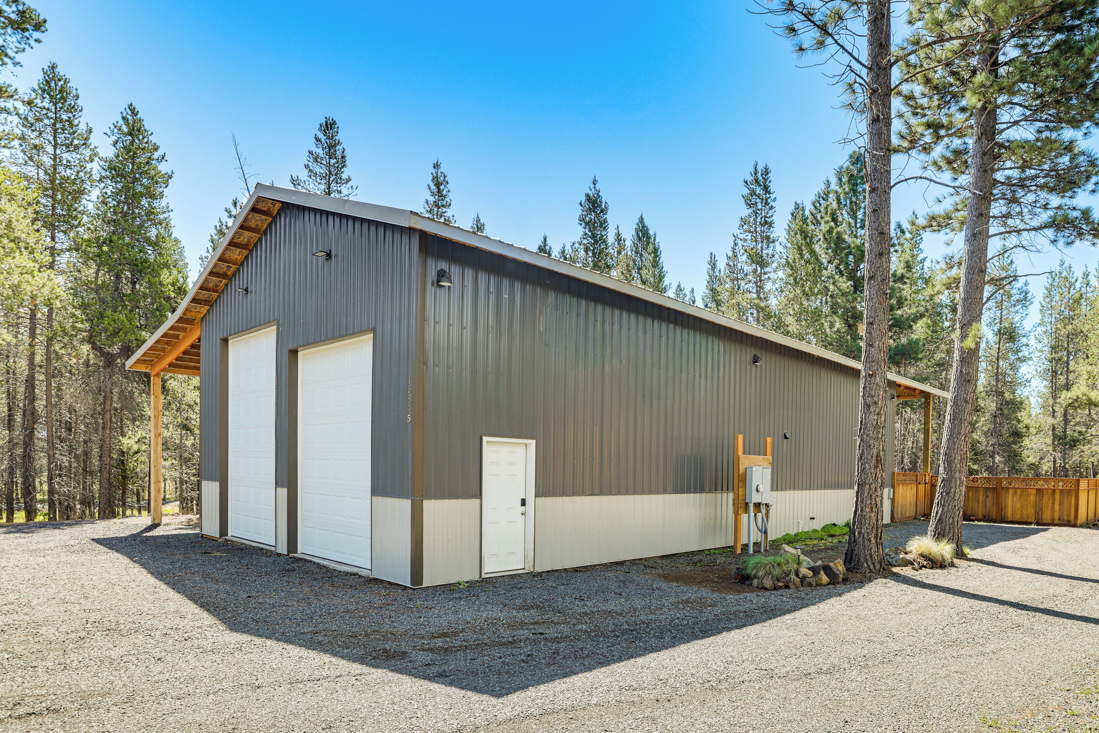 A large, single-story metal building with a garage door, surrounded by trees.