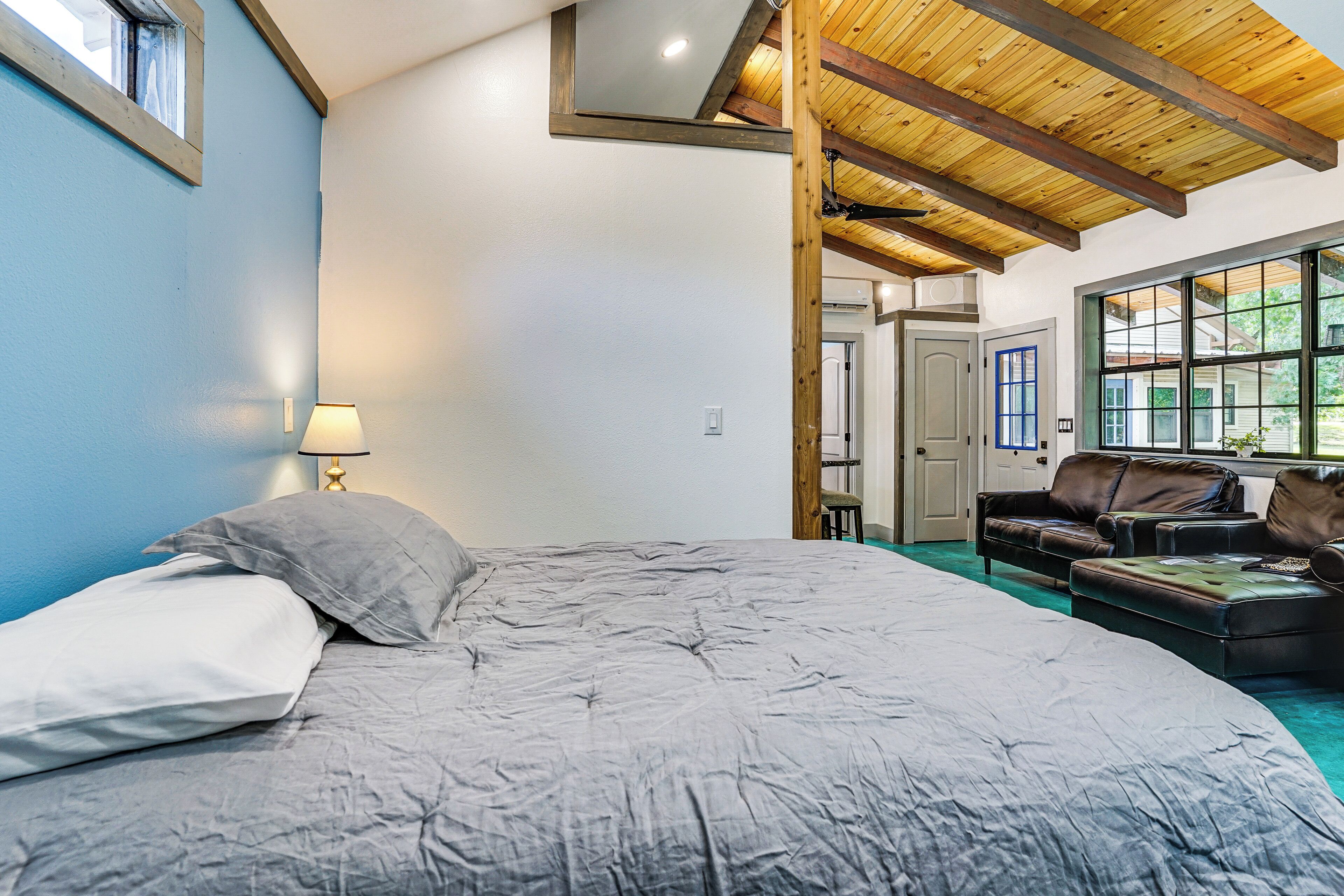 Une chambre à coucher avec un lit, une table de chevet, une lampe, une fenêtre, une porte et une vue sur l’extérieur.