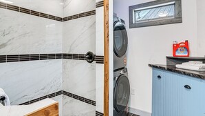 A bathroom with a marble shower, a wooden door, a washing machine, and a blue cabinet. - Paluxy Riverfront Couples Studio on Over 2 Acres! (Glen Rose)